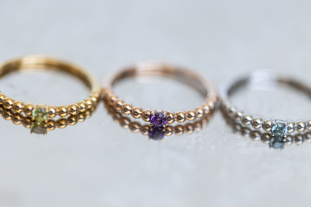 a gold ring with Peridot, a rose gold ring with Amethyst, and a silver ring with Blue Zircon in a row