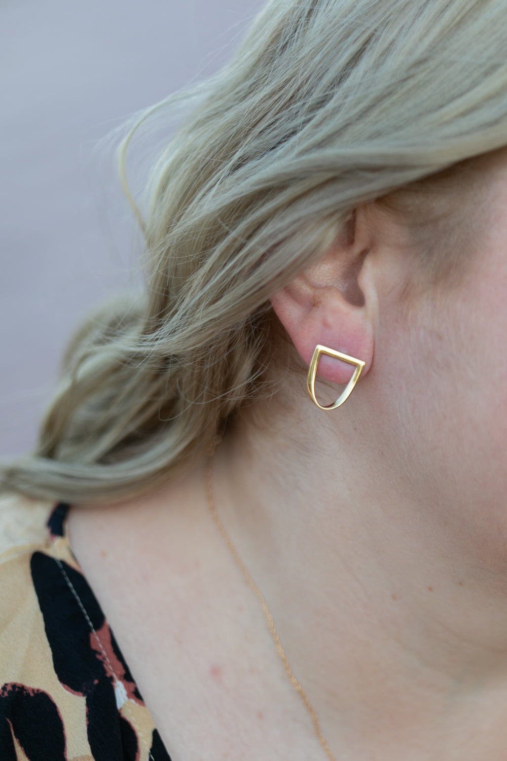 a close up of a blonde wavy haired woman's ear wearing the yellow gold twist earring. #color_gold
