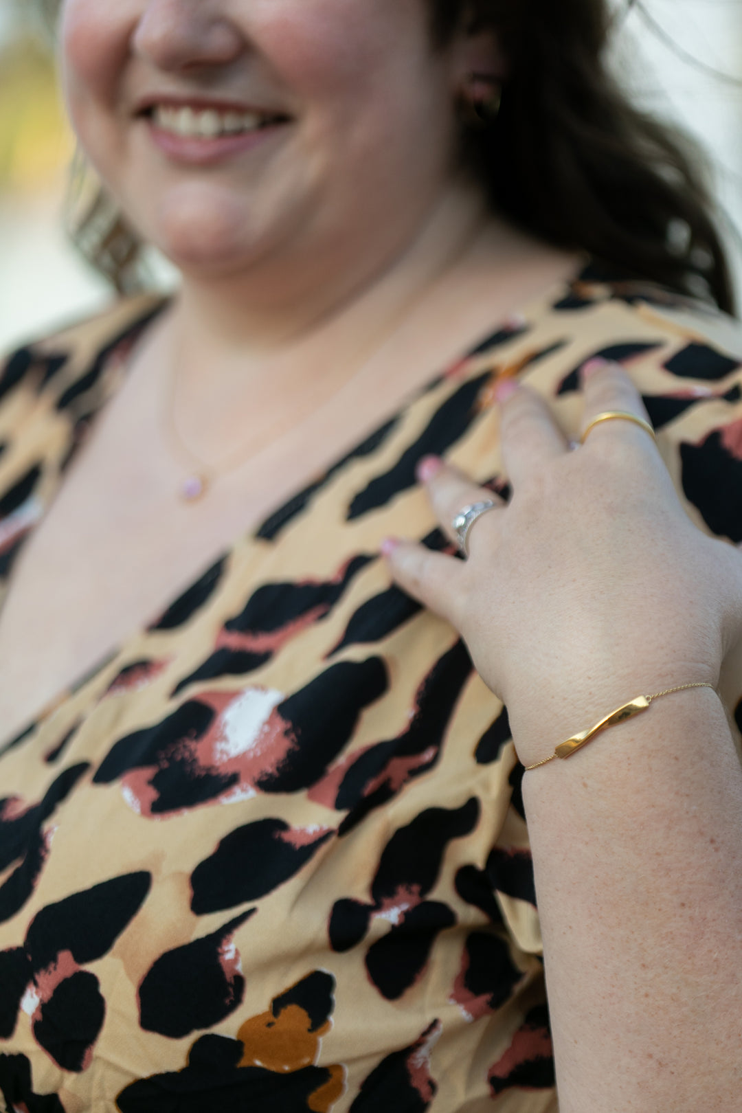 a detailed image of the twist bracelet in yellow gold on a smiling woman in a leopard print dress. #color_gold