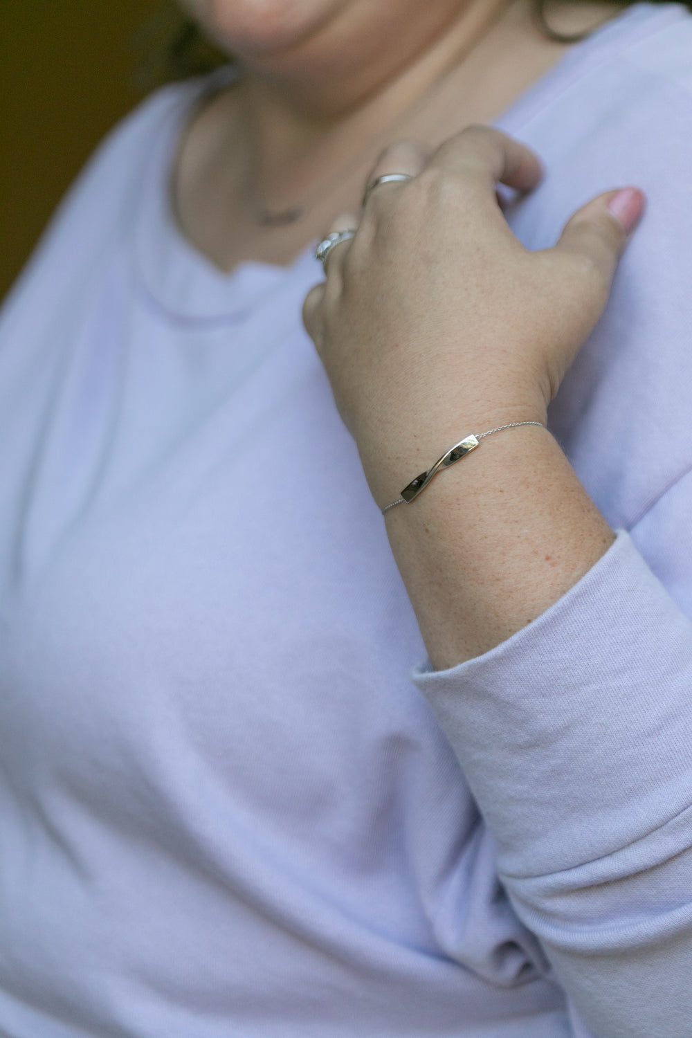 a close up image of a woman's wrist wearing the silver twist bracelet and a light lilac colored sweatshirt. #color_silver