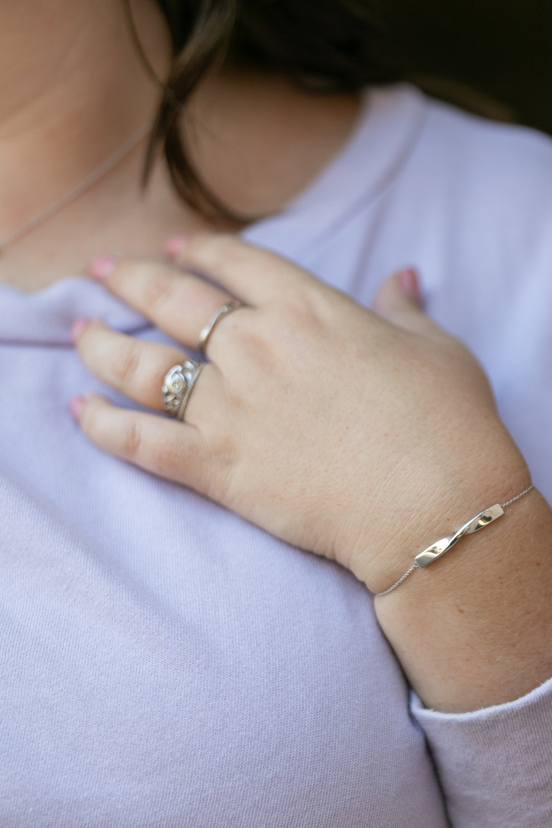 a detailed image of a plus size woman's hand and wrist wearing a twist bracelet in silver and a twist ring in silver. She also wears a lilac colored sweatshirt. #color_silver