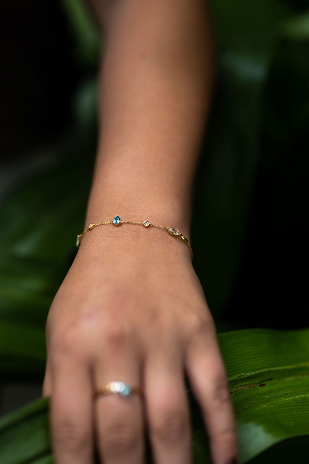 the Monteverde bracelet in gold on a model. Tropical green foliage is visible in the background #color_gold