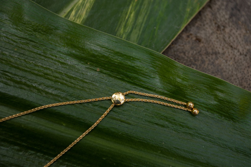 a close up flat lay detailed shot of the bolo closure on a gold Monteverde bracelet atop large green tropical leaves #color_gold