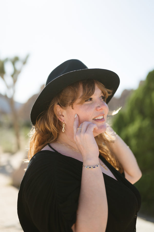 the earrings featured on a model with the warm ember bracelet. A desert scene is visible in the background