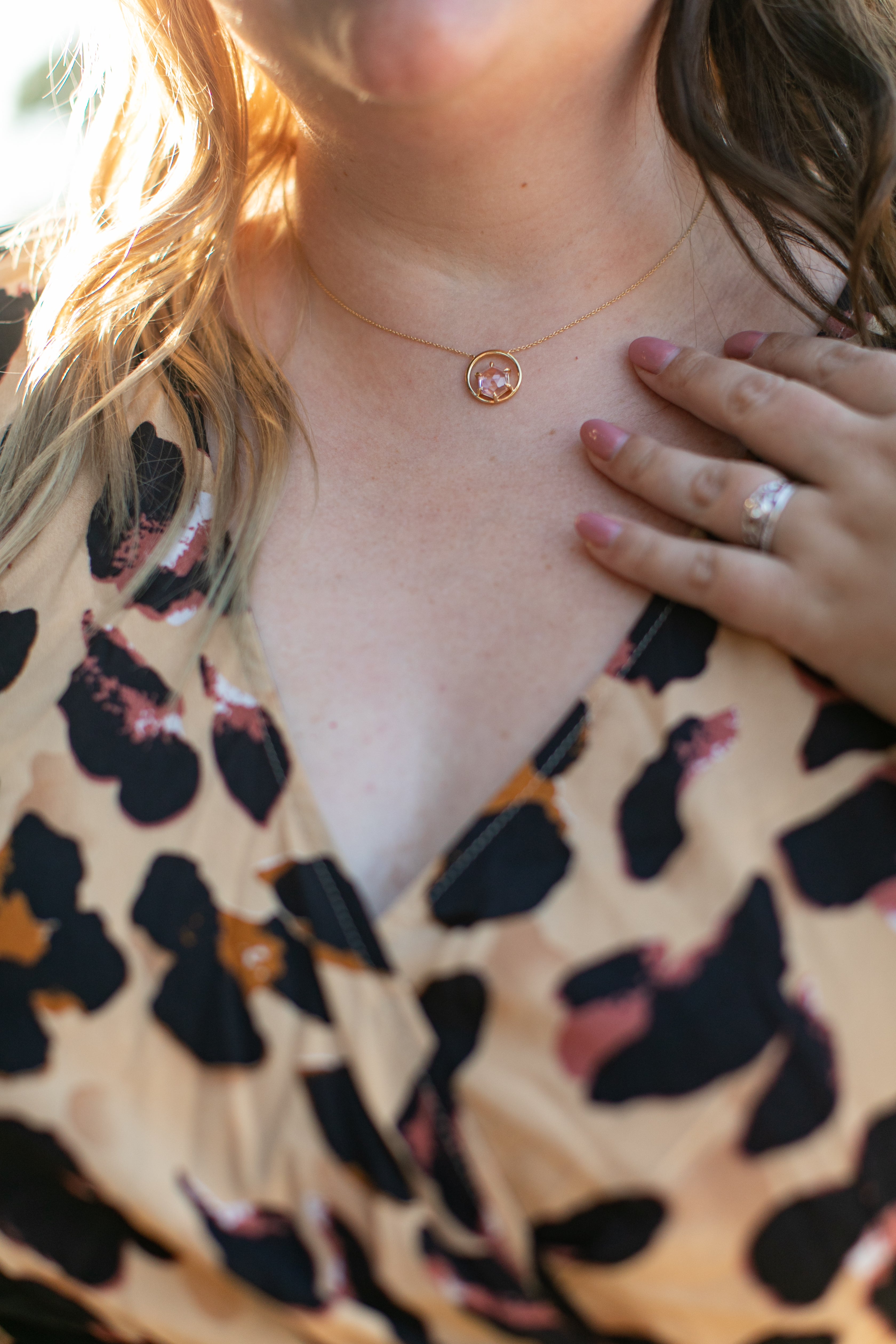 an image of a woman's neck with a gemstone necklace in gold and pink spinel on. She is wearing a leopard print dress.