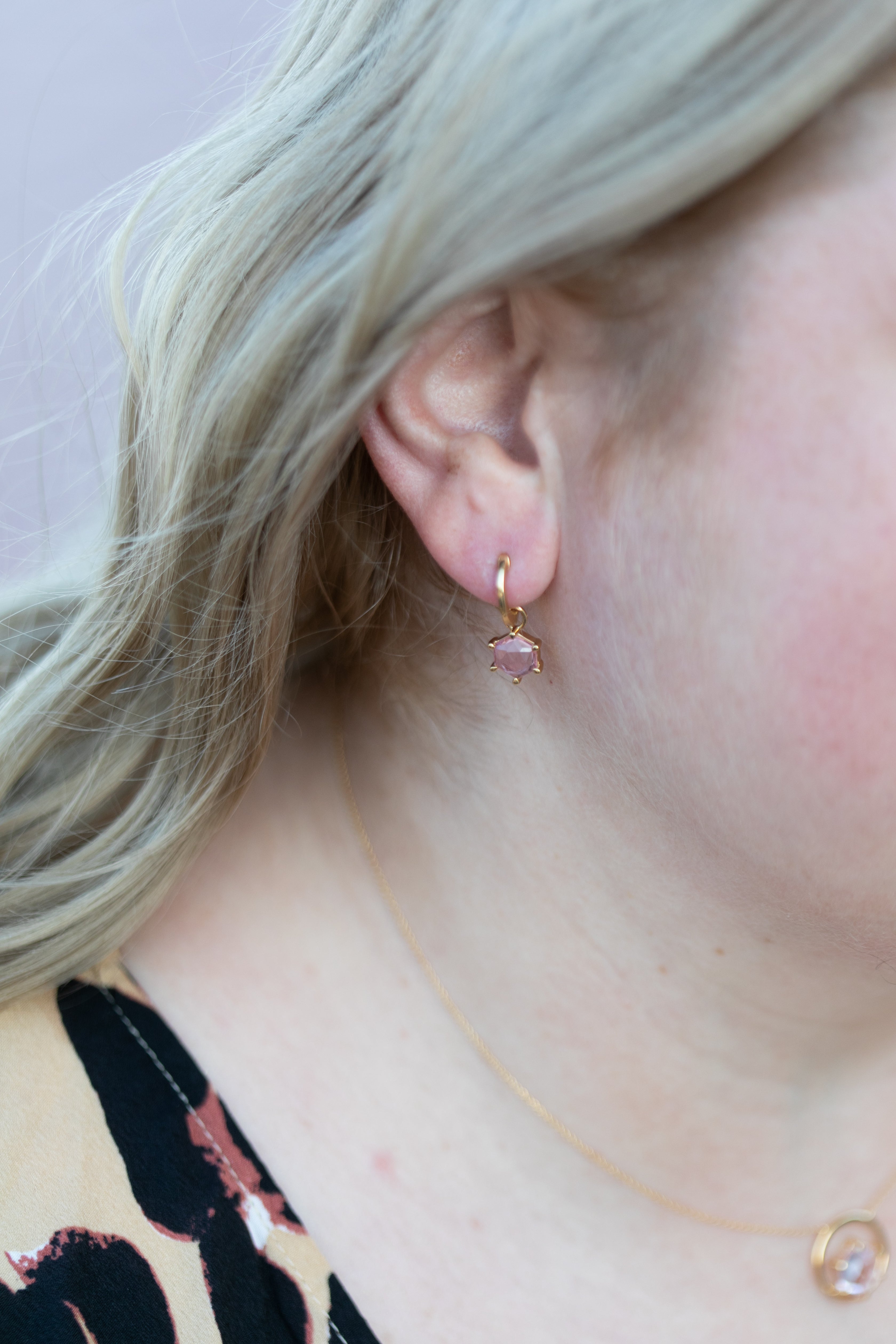 A close up shot of a blonde woman's ear wearing a gemstone huggie hoop in gold and spinel.