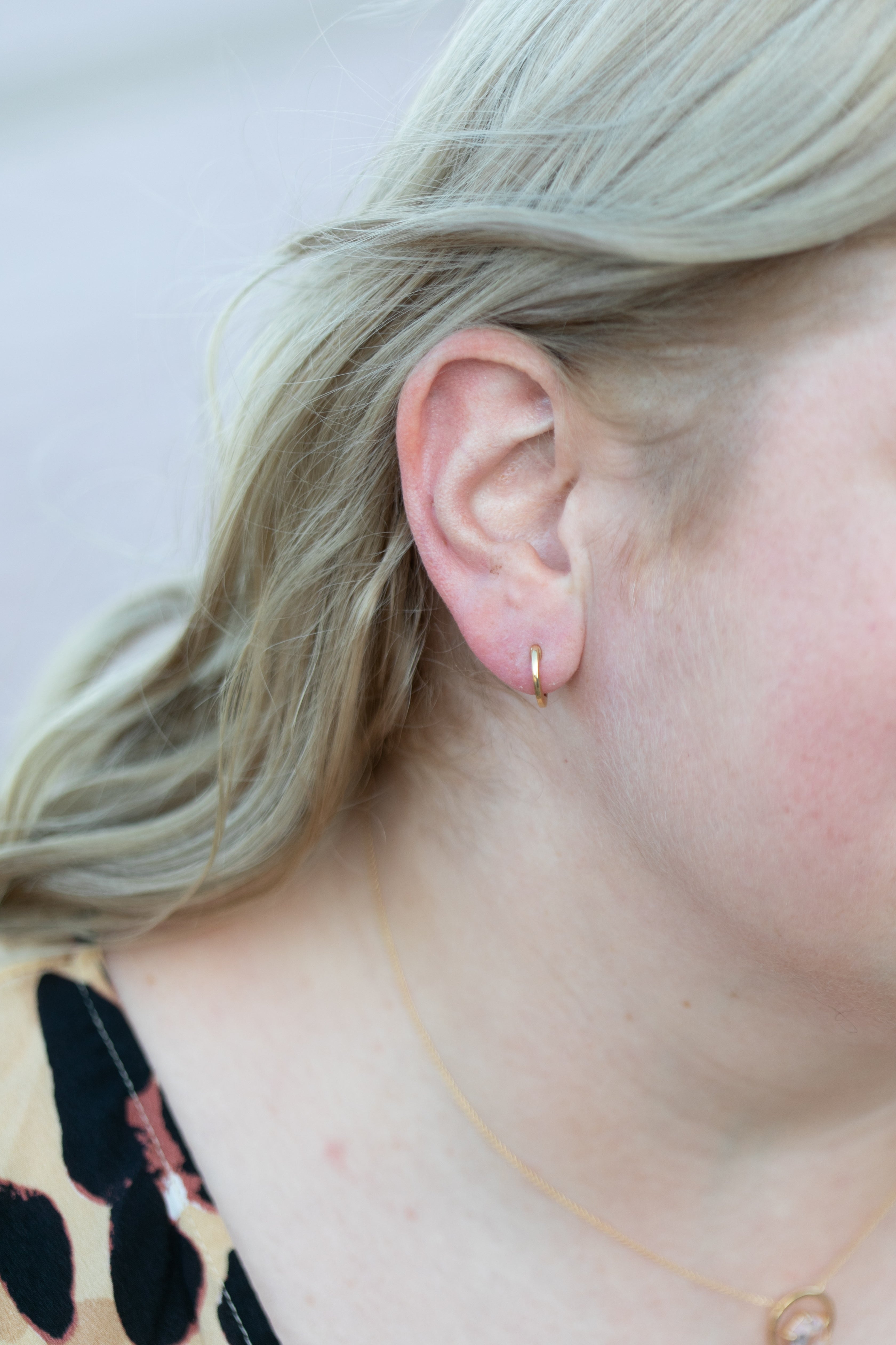 A close up shot of a blonde woman wearing the gemstone huggie hoop with the gemstone removed, so it is just a plain gold earring.