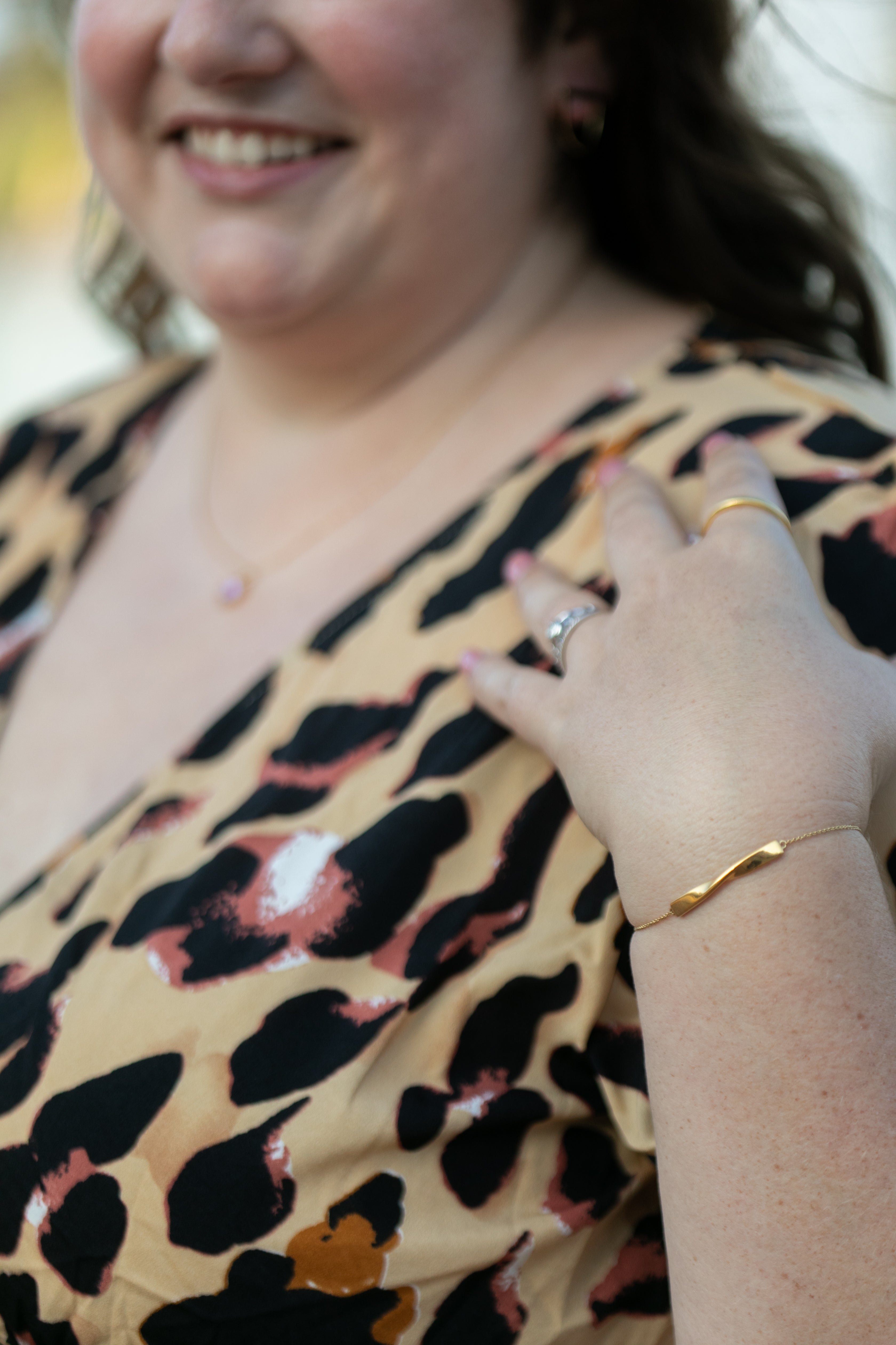 a detailed image of the twist bracelet in yellow gold on a smiling woman in a leopard print dress.