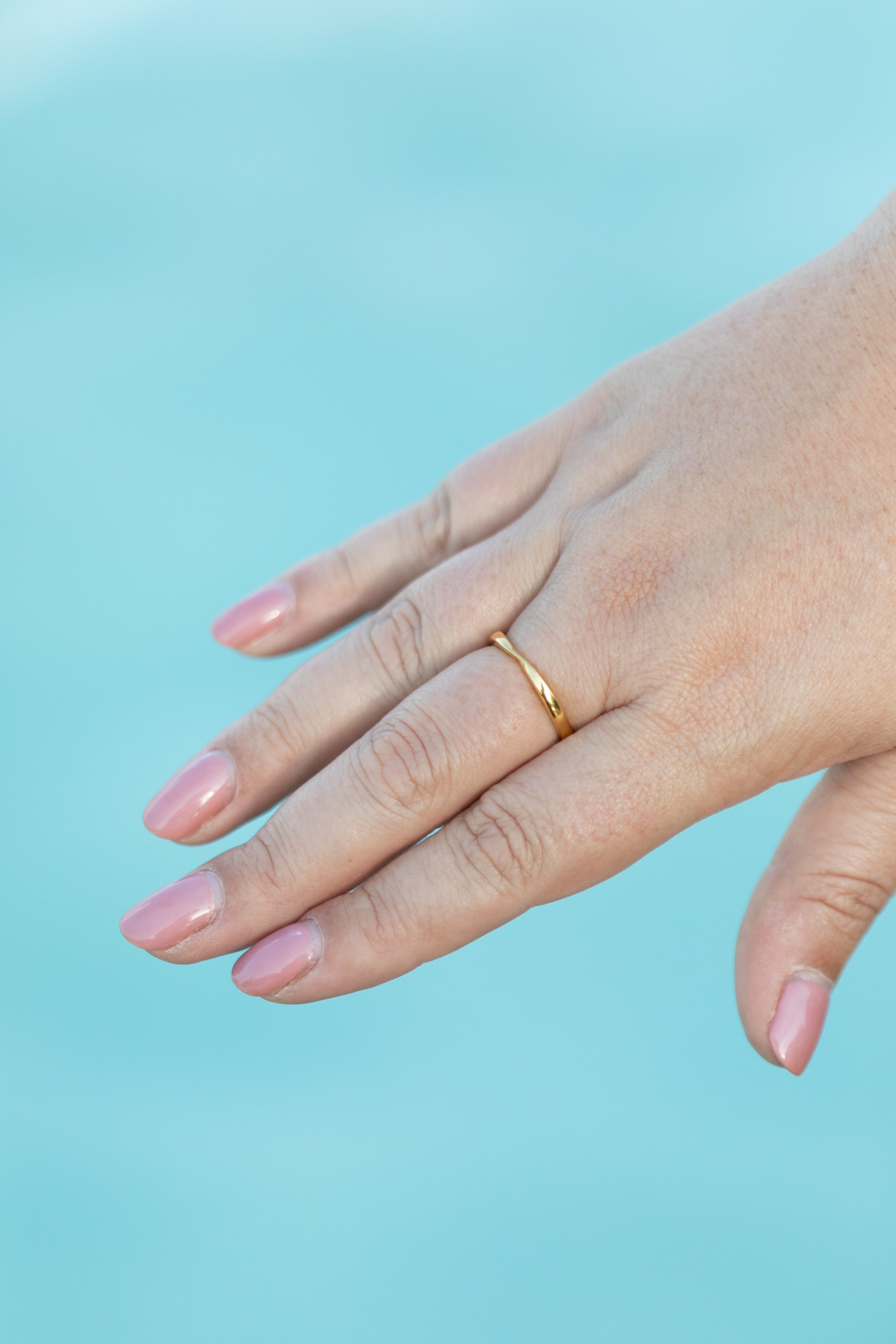a plus size woman's hand is held above a bright blue fountain wearing a simple gold twist ring.
