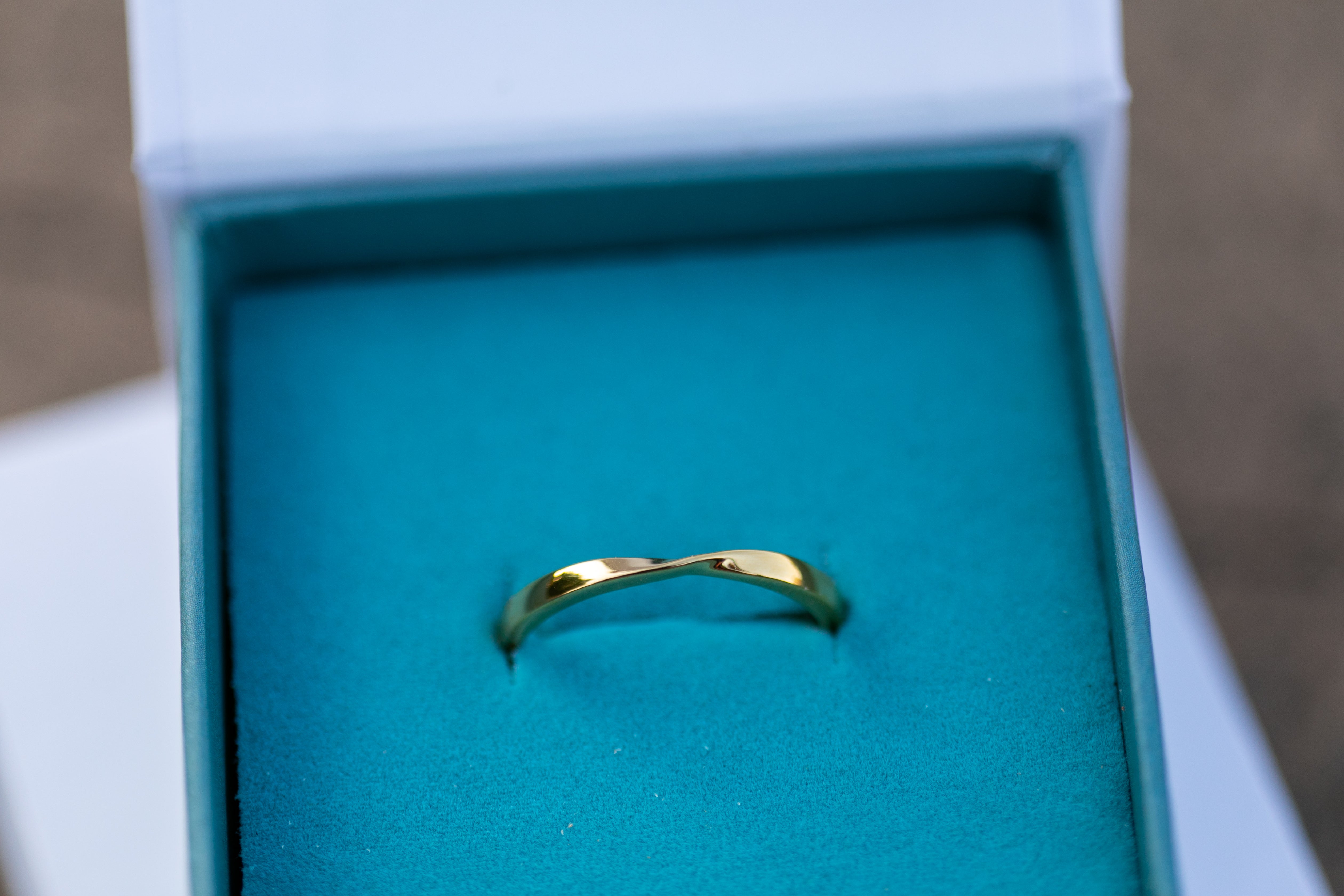 a close up shot of a gold twist ring sitting in a teal Chouette Designs branded ring box