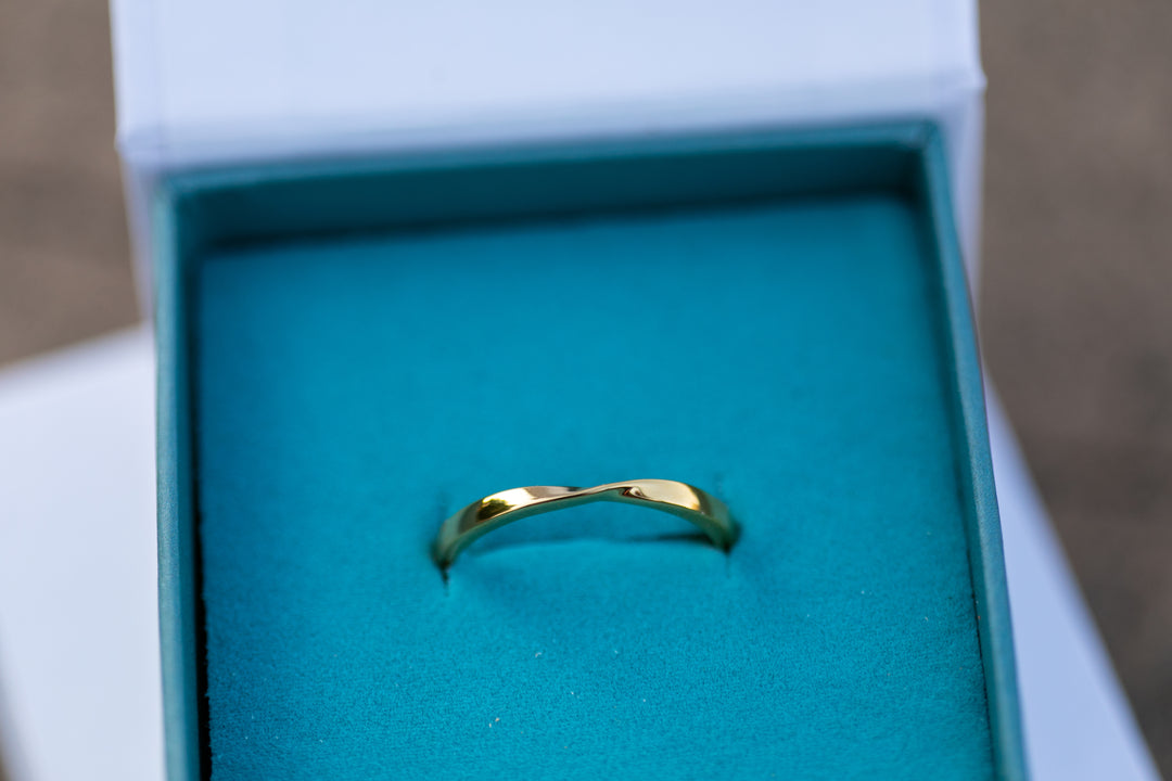 a close up shot of a gold twist ring sitting in a teal Chouette Designs branded ring box 