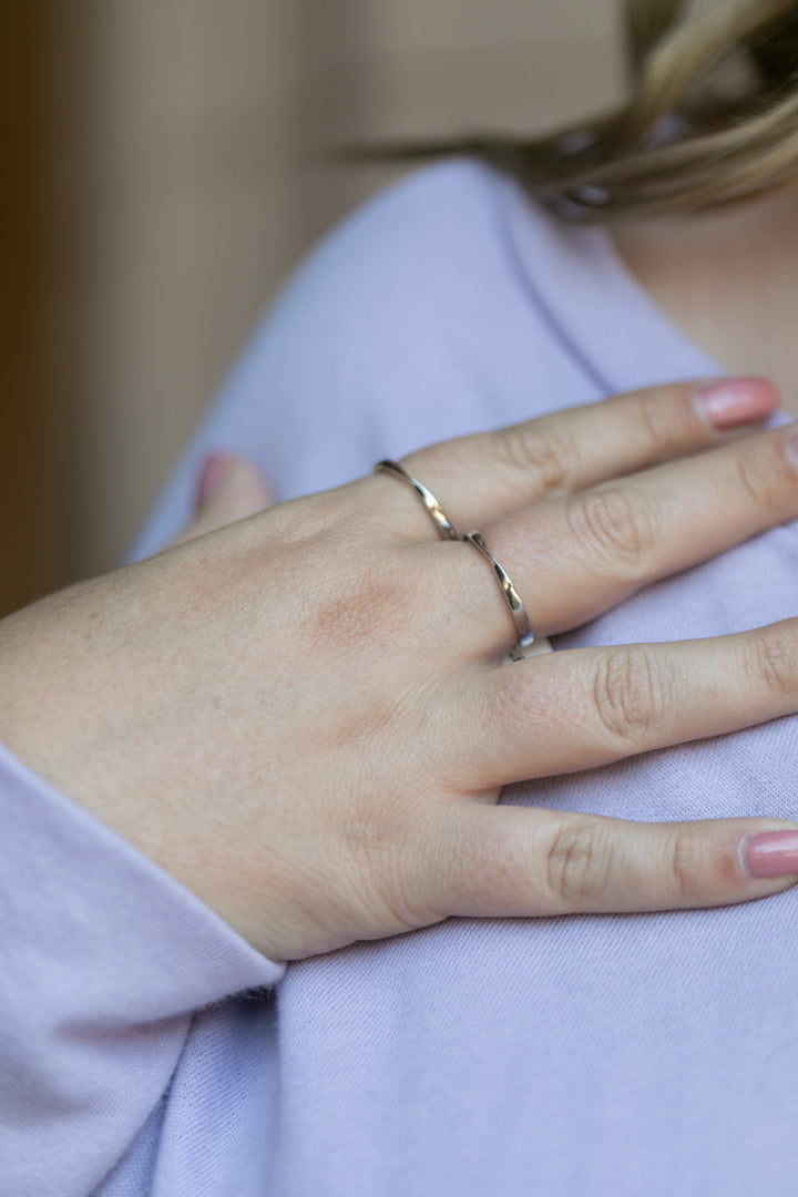 A close up of a woman's hand with a twist ring in silver on her pointer and middle fingers 