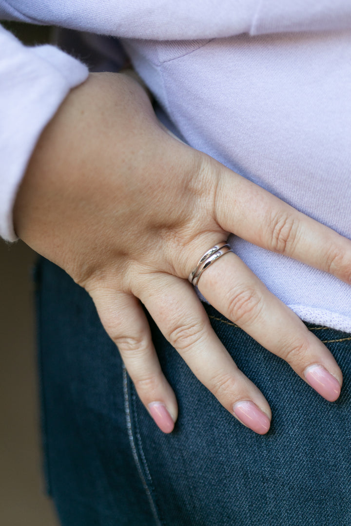 a close up of a plus size woman's hand wearing two stacked twist rings in silver on her middle finger with her thumb in her blue jeans.  