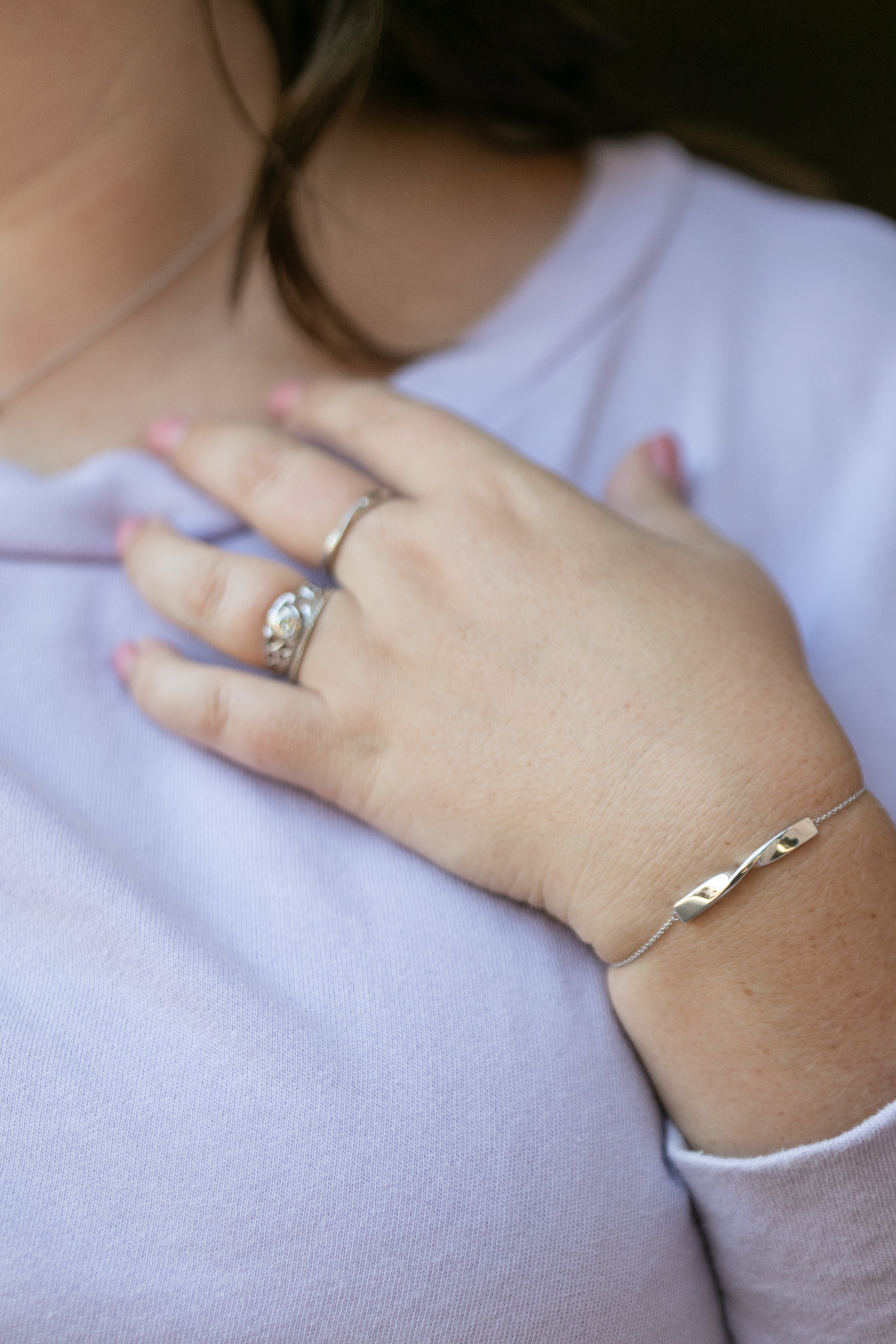 a detailed image of a plus size woman's hand and wrist wearing a twist bracelet in silver and a twist ring in silver. She also wears a lilac colored sweatshirt.