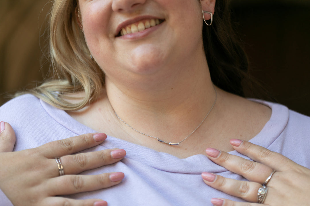 close up of a woman smiling from the nose down, with her hands on her chest, showing off silver twist rings and a twist necklace. She is also wearing silver twist earrings. #color_silver