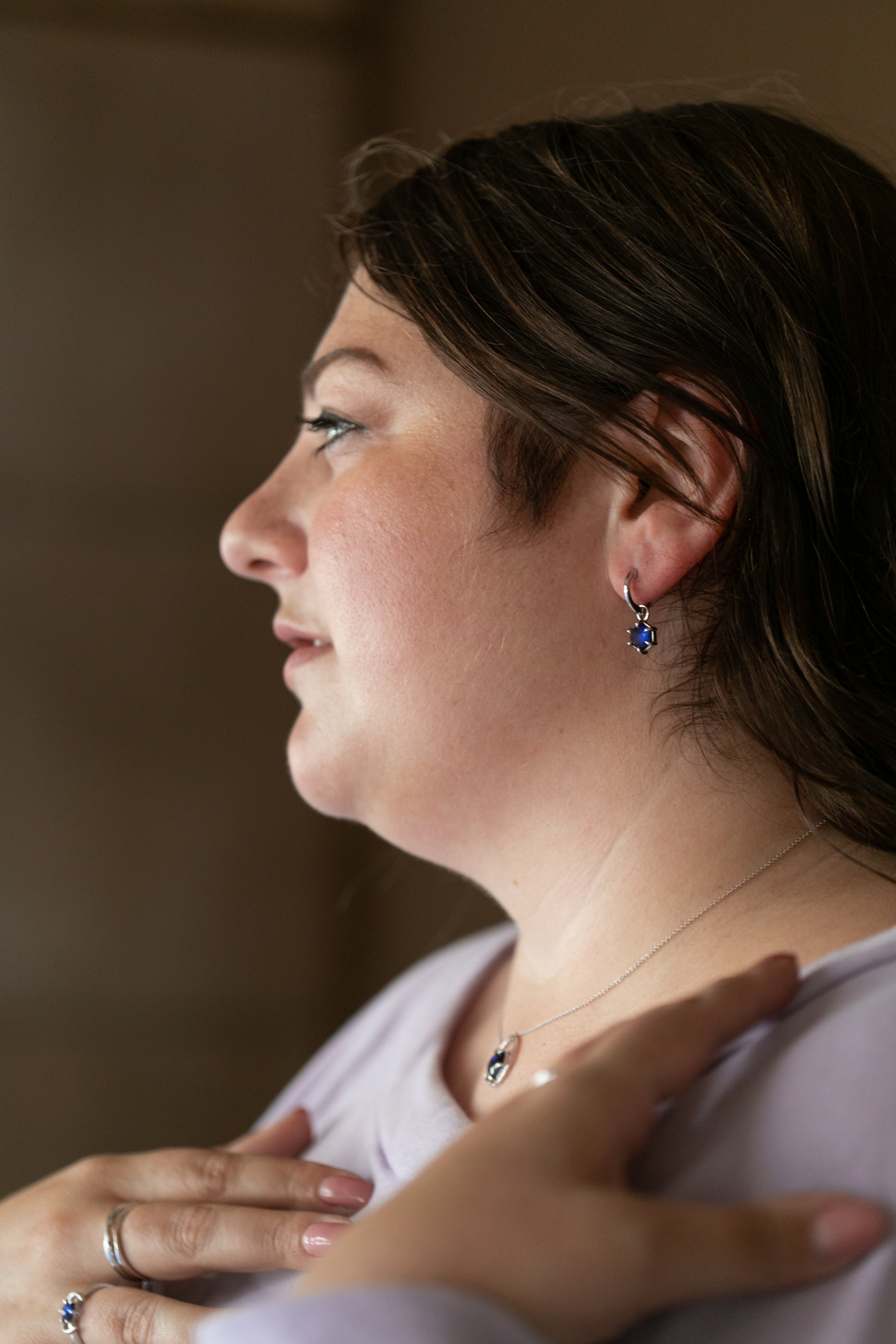 A profile of a brunette plus size woman wearing the silver and tanzanite huggie hoops, gemstone necklace and silver rings.