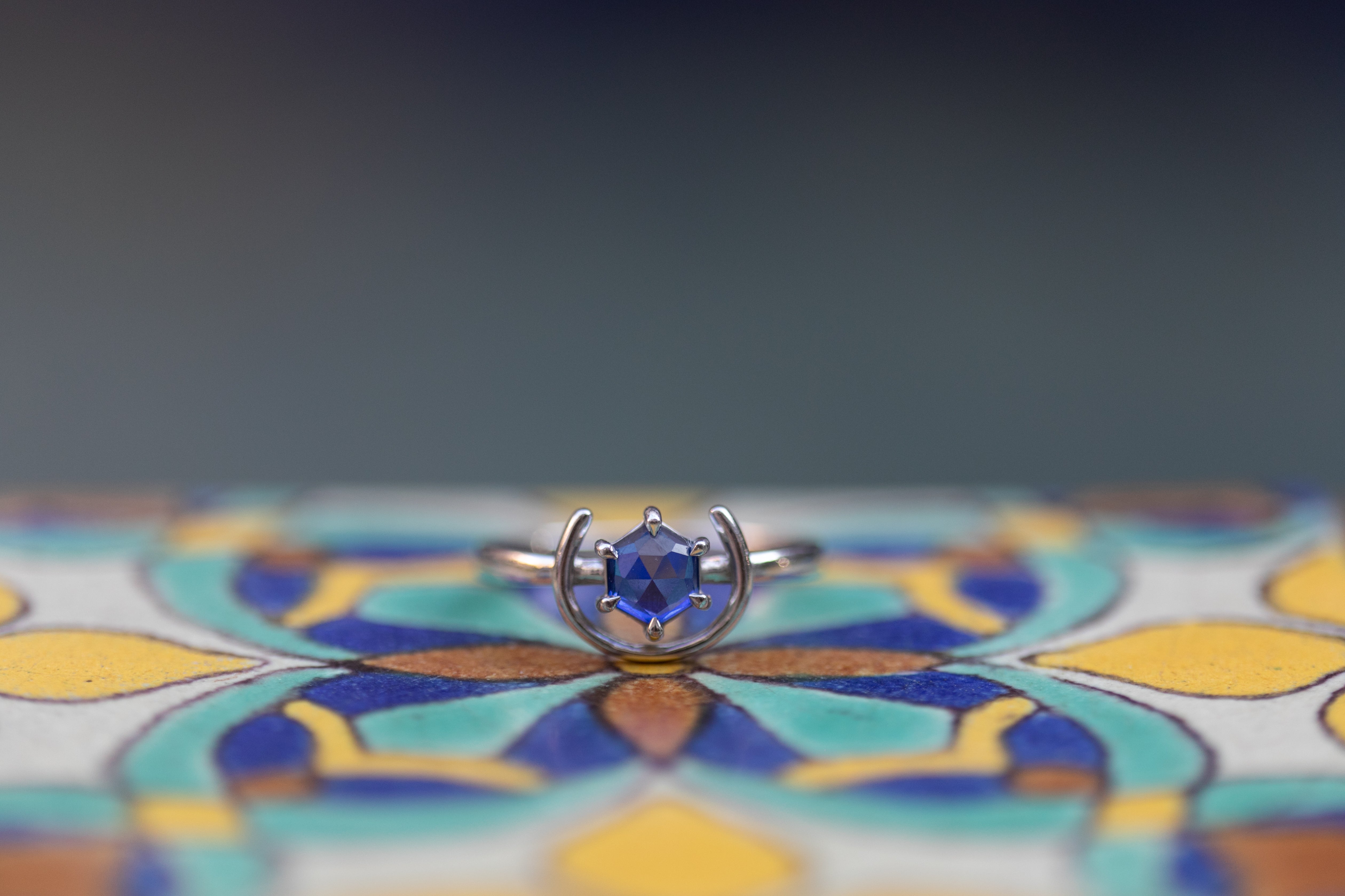 a detail shot of the gemstone ring in silver and tanzanite sitting atop a colorful Spanish style tile. Plus size, size inclusive ring.