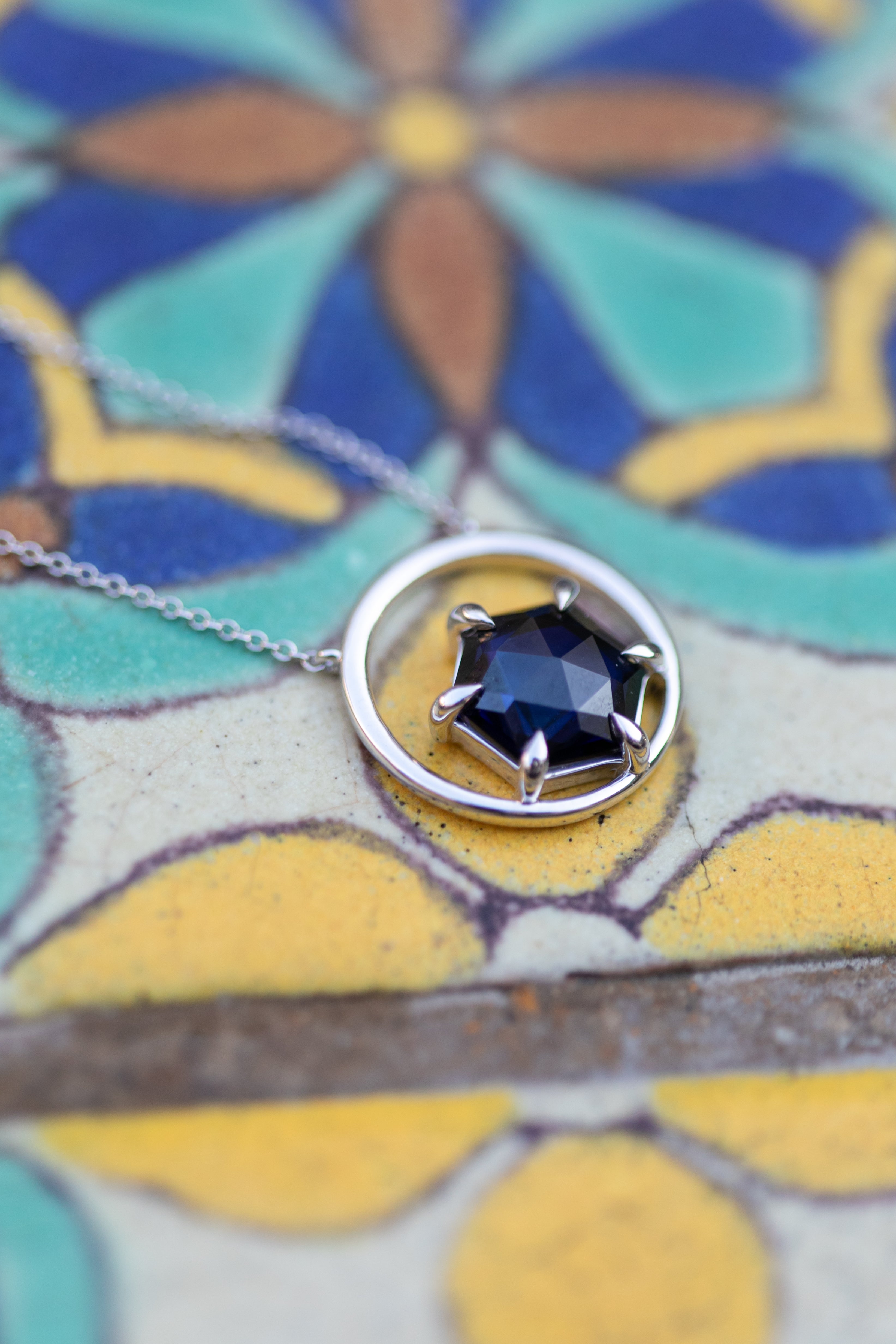 A close up shot of the gemstone necklace in silver and tanzanite laying on a colorful Spanish tile.