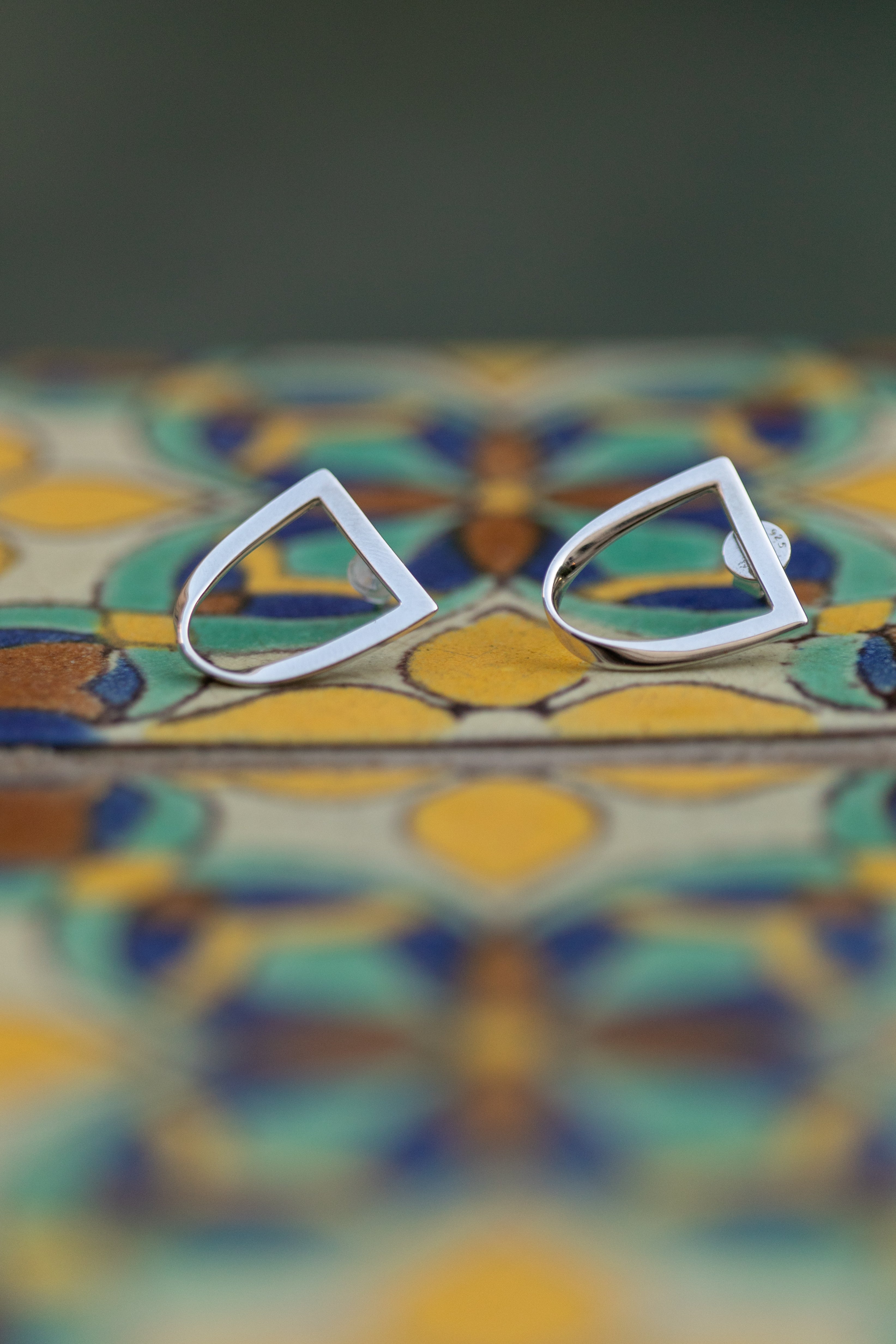 a pair of silver twist earrings sit atop a colorful Spanish style tile.