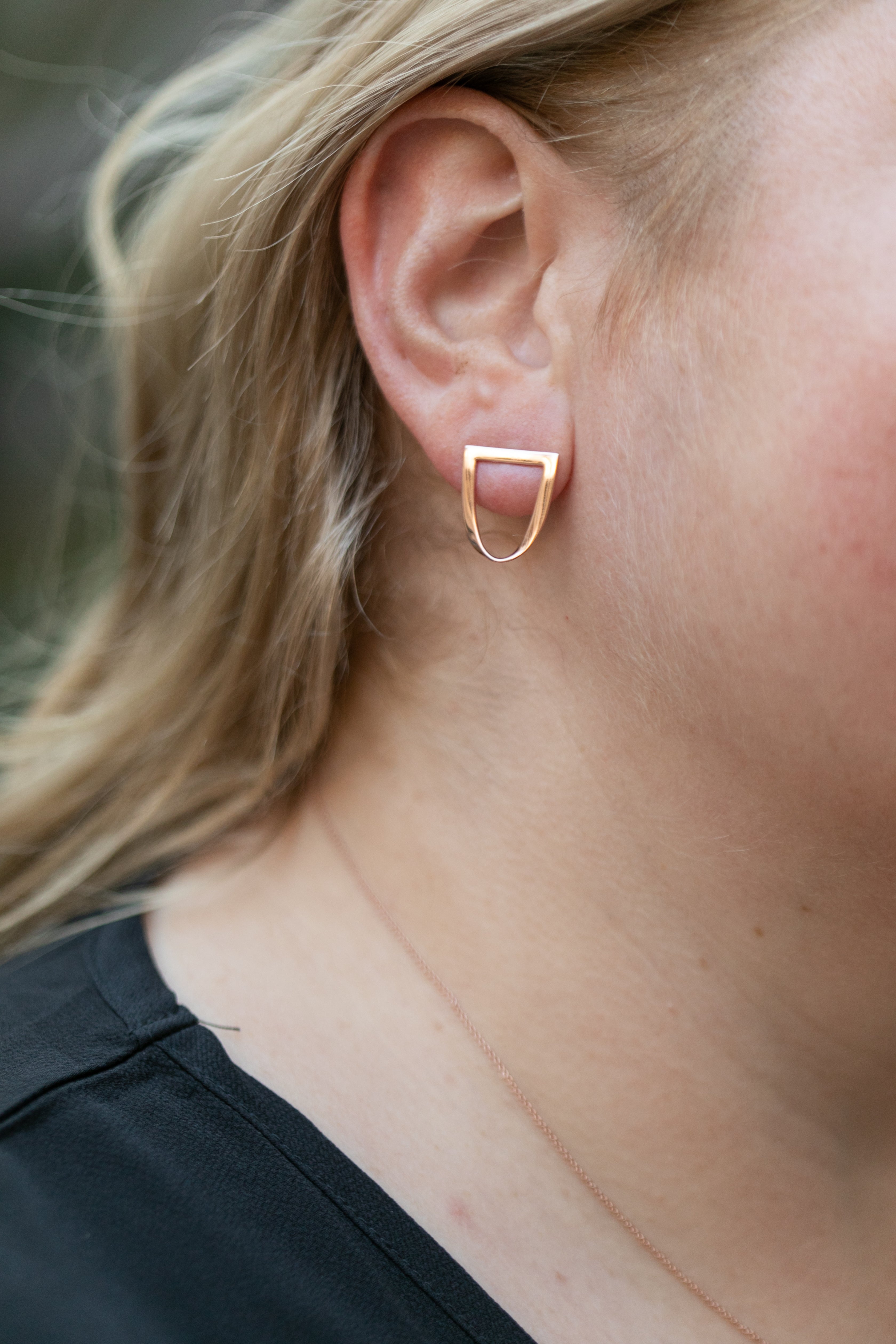 a close up of a blond woman's ear with a twist earring in rose gold