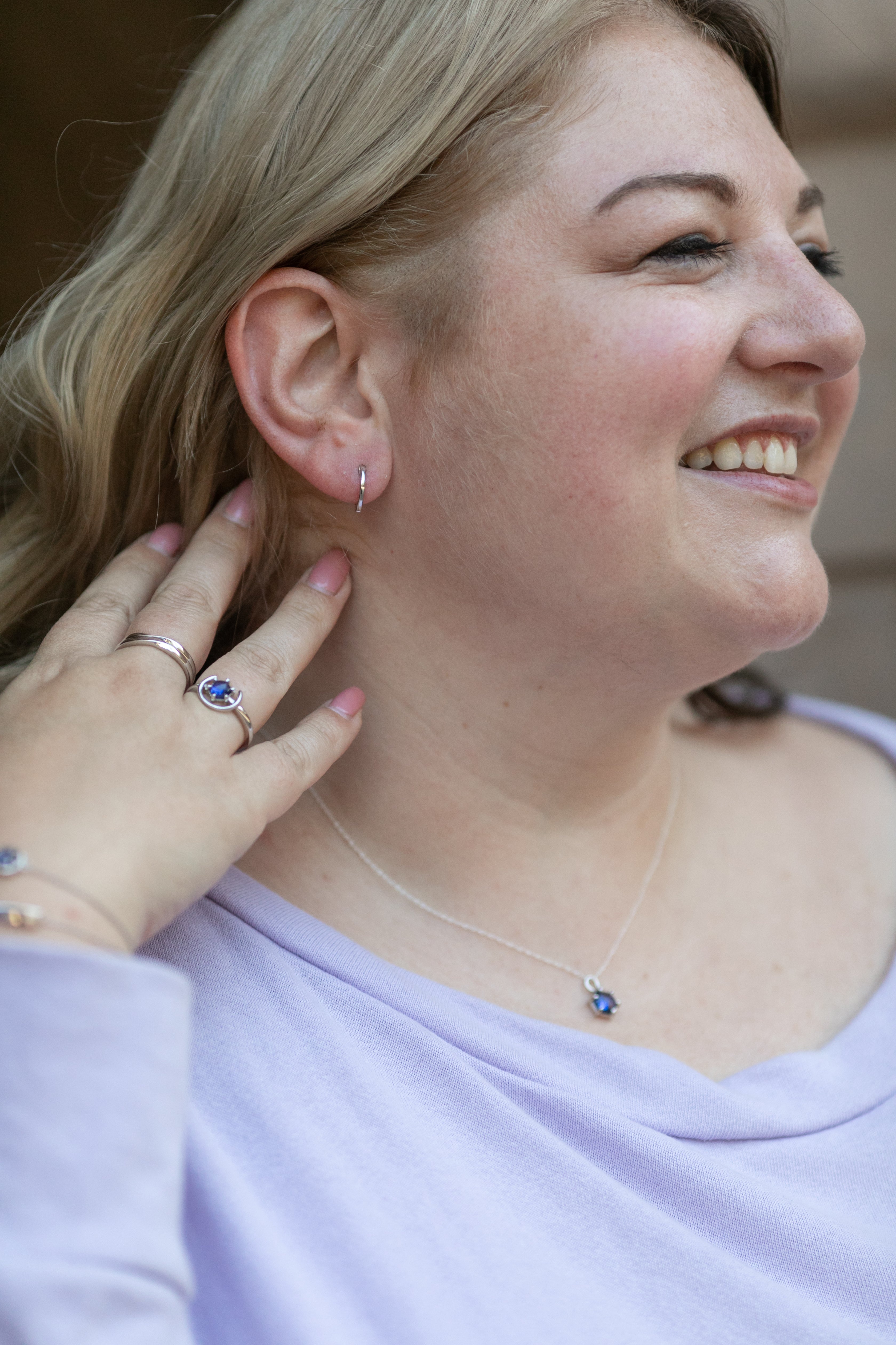 a profile of a blonde woman smiling with a simple huggie hoop earring, tanzanite and silver rings, and tanzanite and silver necklace on.