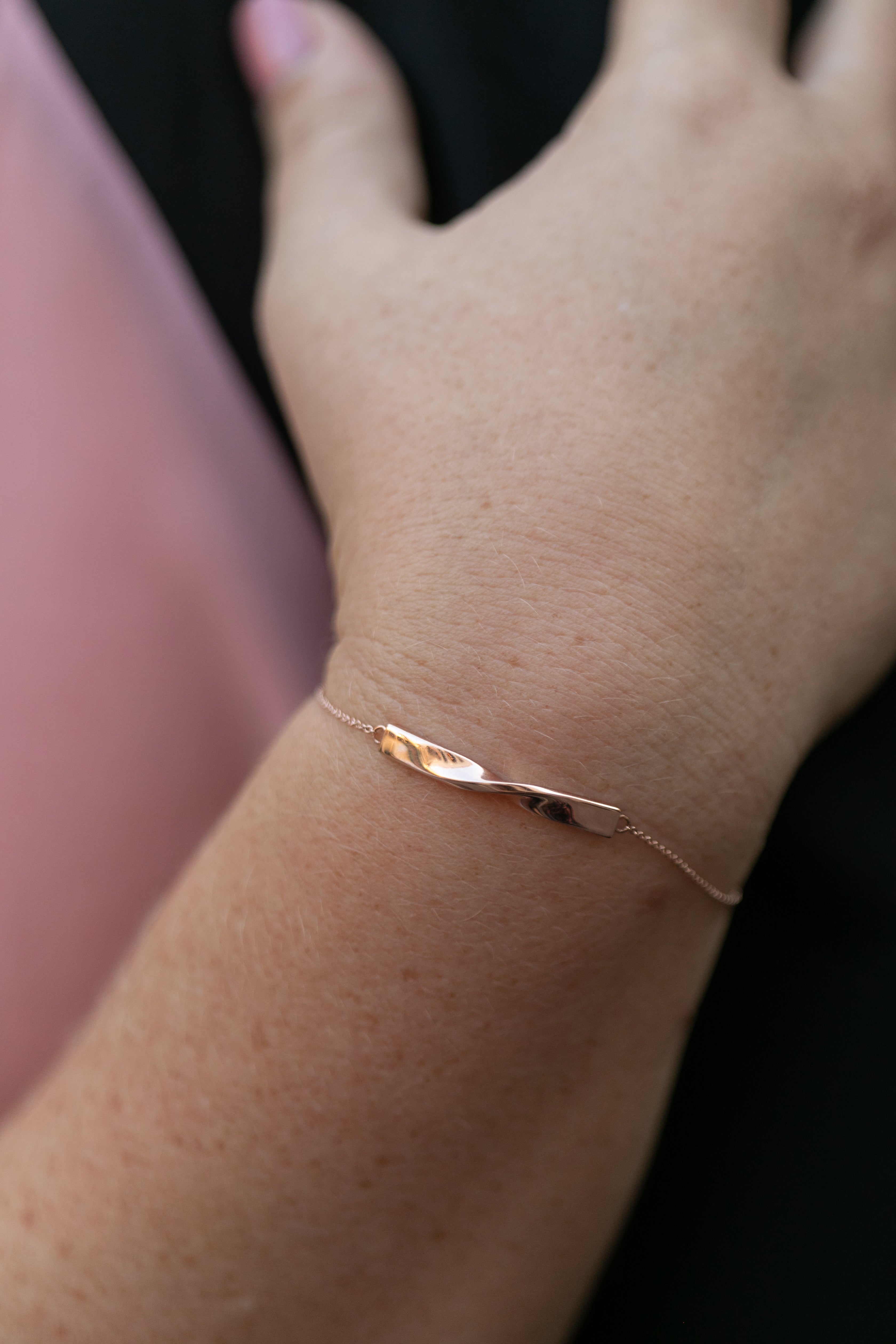 a close up shot of a rose gold twist bracelet on a person wearing black and pink.