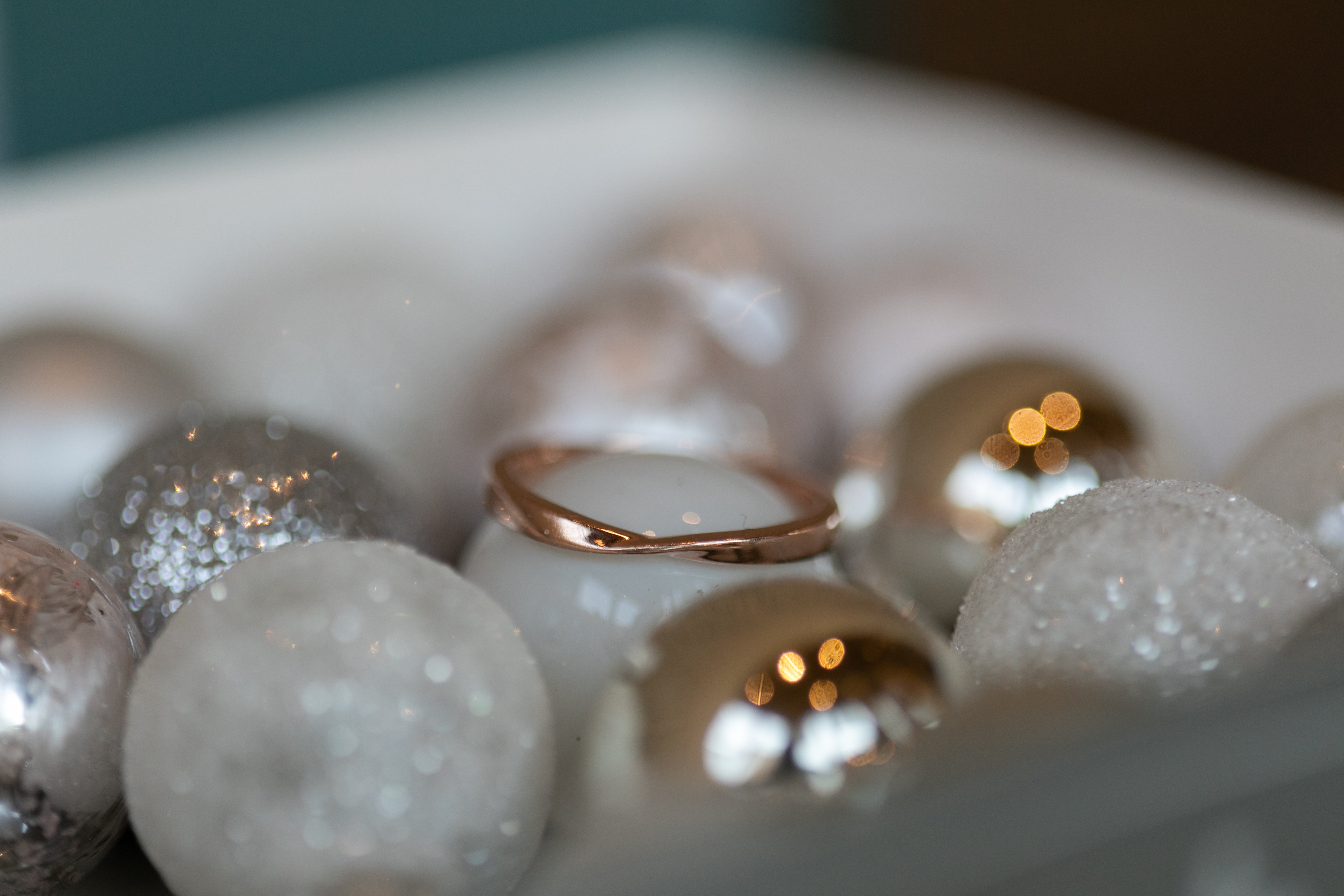 a rose gold twist ring sits atop a white Christmas ornament, nestled among other ornaments in silver and white.