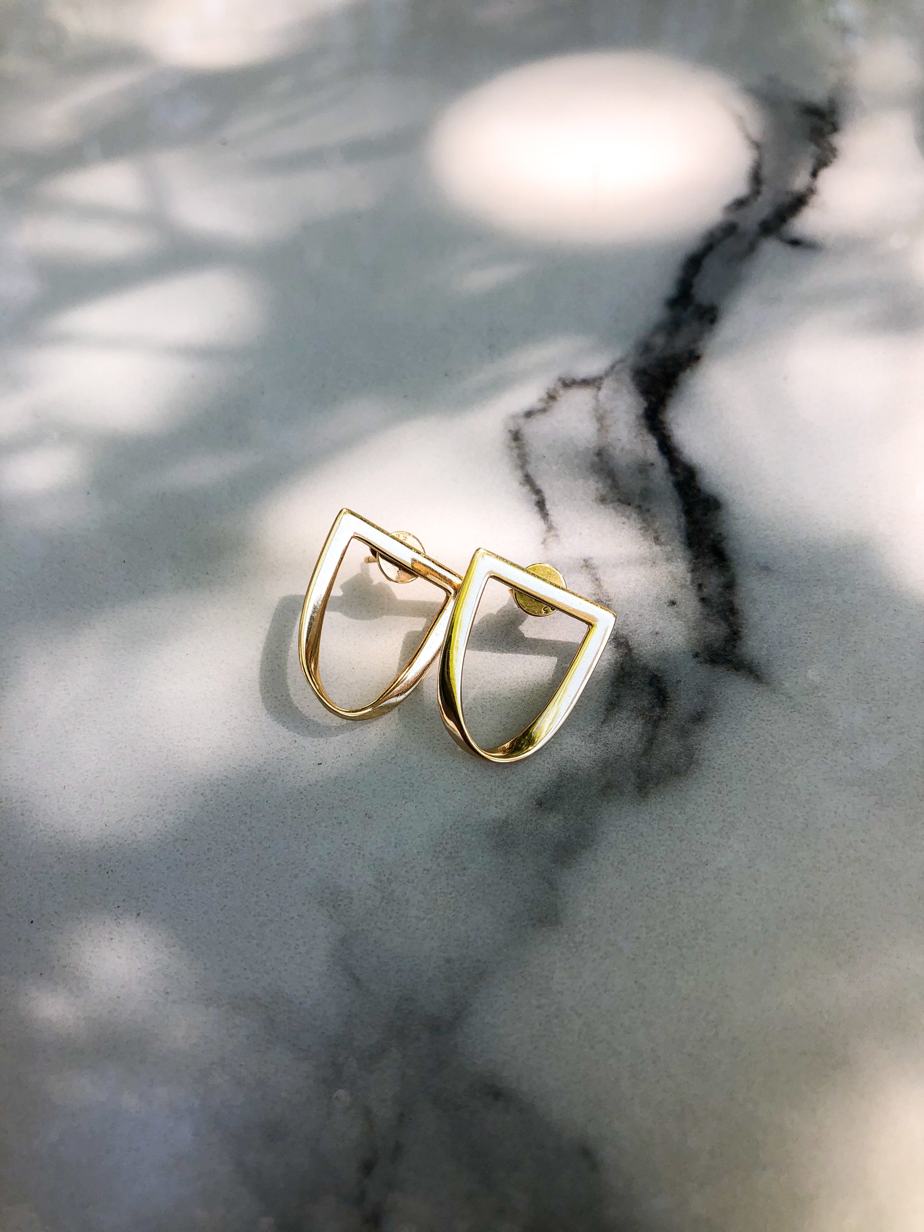 a pair of twist earrings in yellow gold sit atop a marble table top with speckled shadows across it.