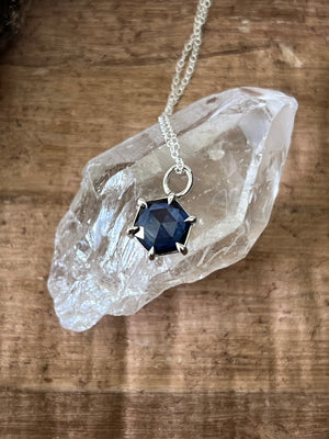 a close up of a silver and tanzanite necklace draped across a clear quartz crystal