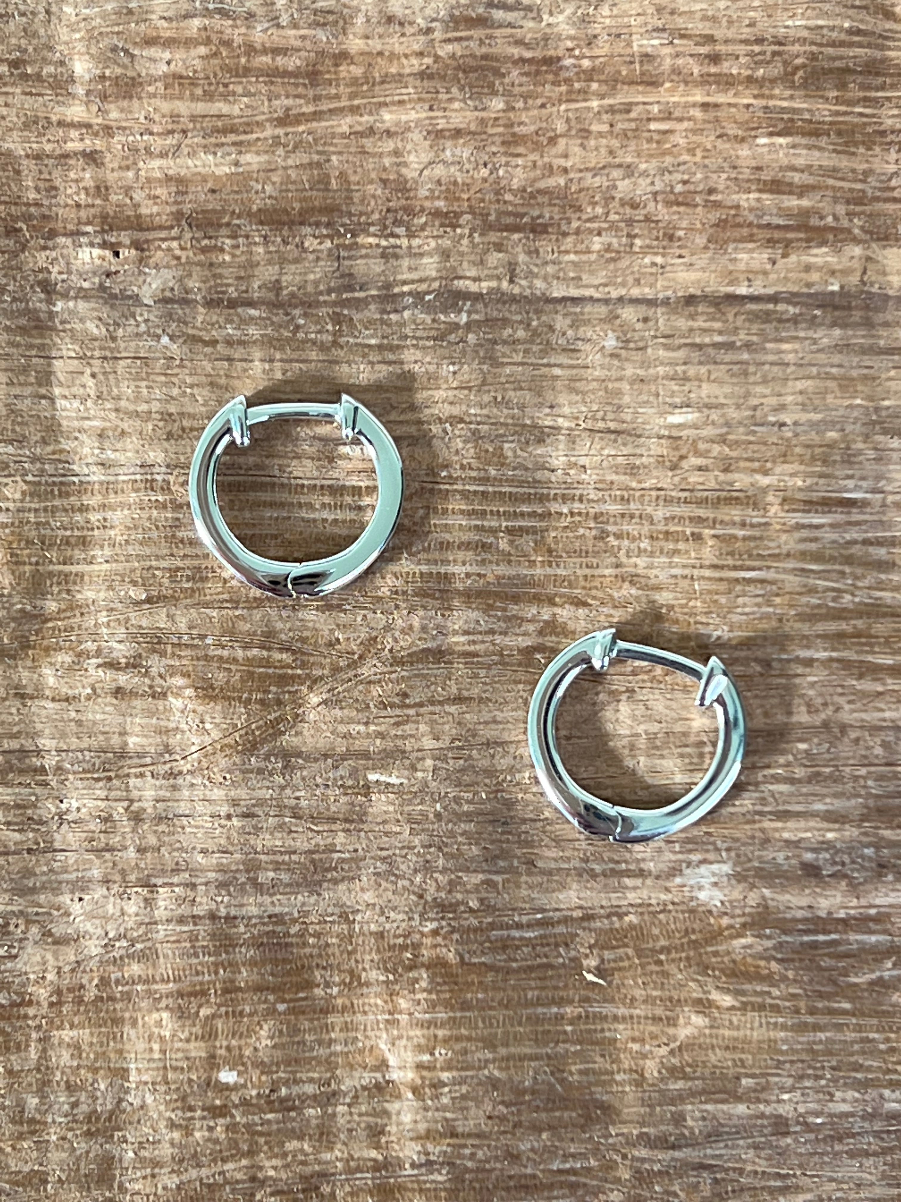 a detail image of two simple huggie hoop earrings in silver laying on a wood grain backdrop